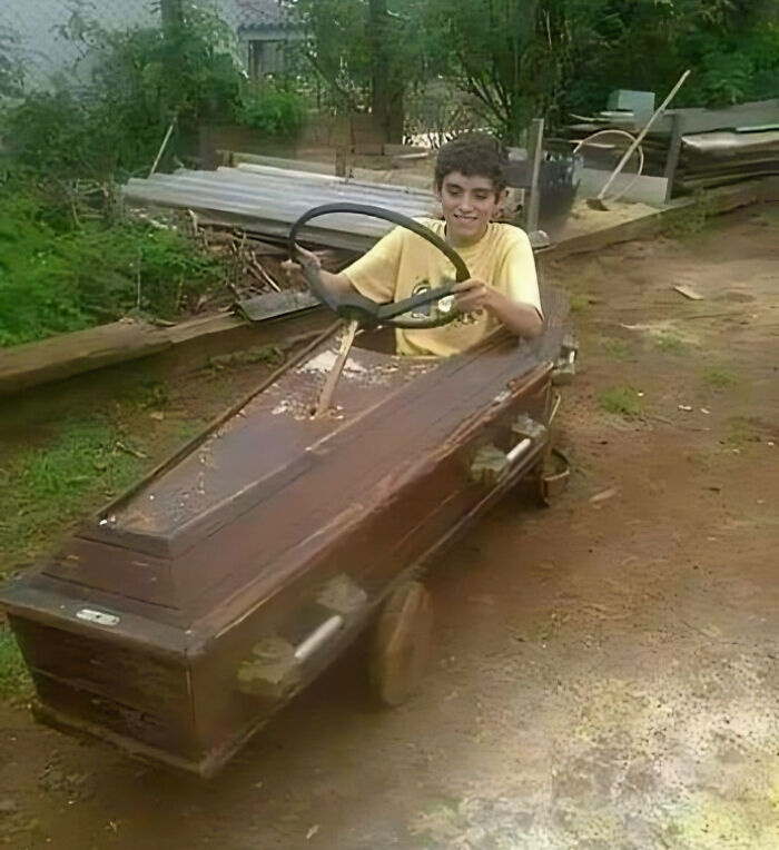 Boy in a coffin-shaped go-kart with a steering wheel, creating a hilarious and unexpected image.