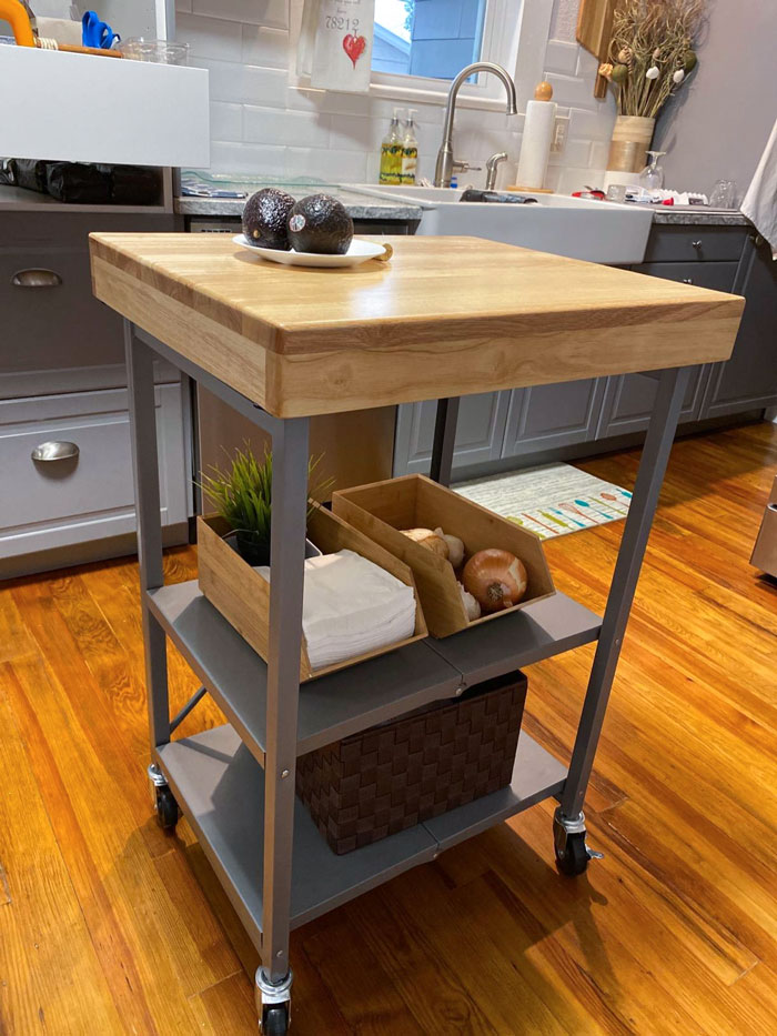 Small rolling kitchen cart with wood top and storage shelves holding vegetables and a plant in a tiny apartment furniture find.