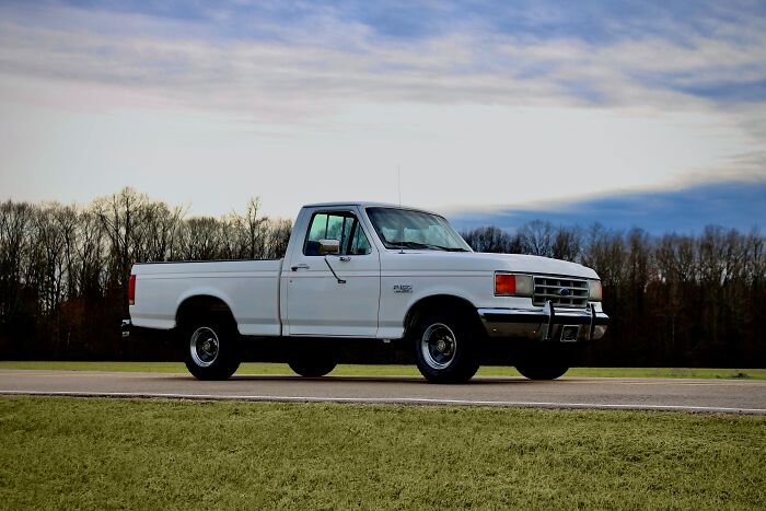 White pickup truck parked on a rural road with a background of trees and a cloudy sky, representing memorable strangers.