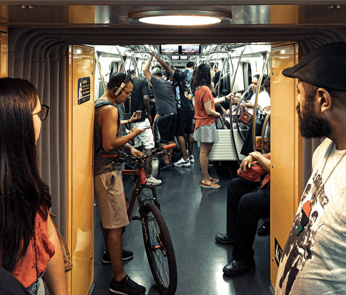 Passengers, including a cyclist and commuters, interacting and standing inside a crowded subway car with memorable strangers.