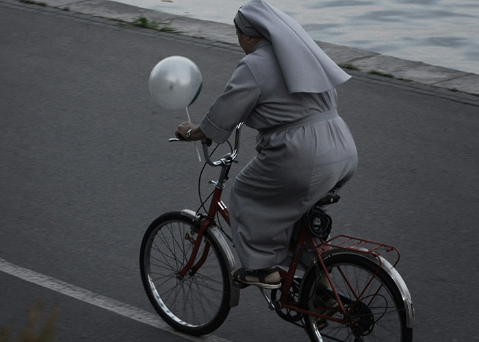 A nun rides a bicycle with a balloon attached, creating a funny scene.