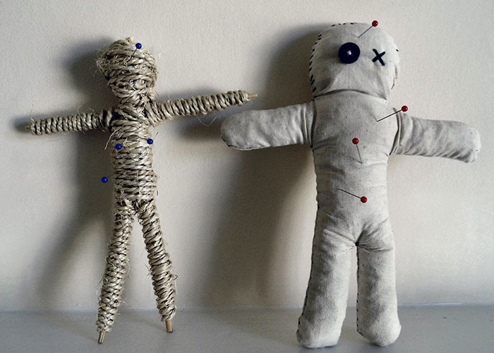 Two humorous voodoo dolls with pins, standing side by side against a plain background.