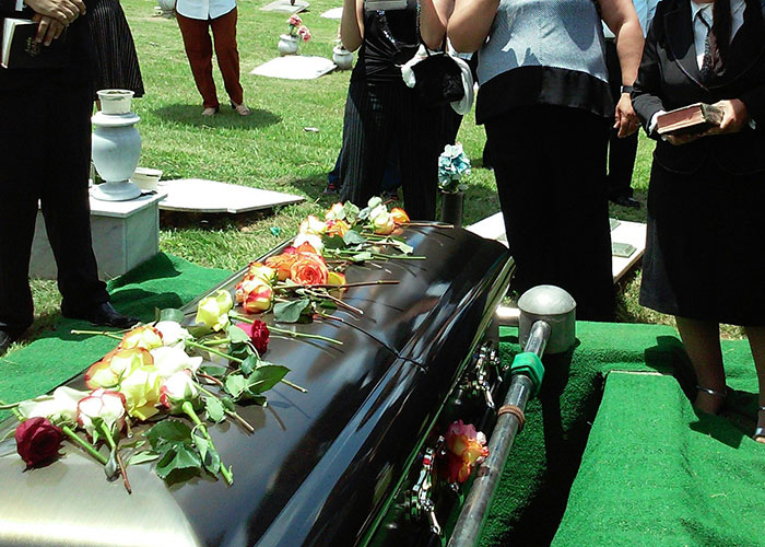 A coffin at a cemetery with flowers, surrounded by people in formal attire.