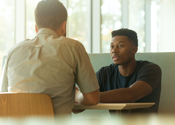 Two men sitting in a casual setting, engaged in conversation about jokes and humor.