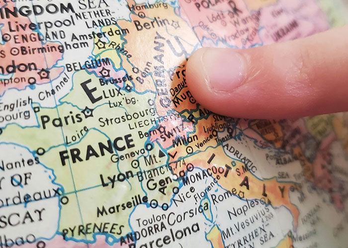 Finger pointing at Europe on a globe, highlighting France, Germany, and Italy, a playful geography reference.