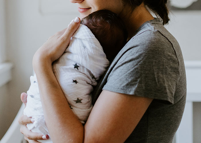 A person in a gray shirt gently cradling a swaddled baby in a cozy room setting.