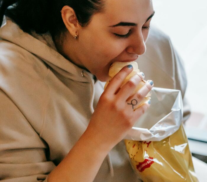 Person in a beige hoodie struggling to eat a chip from a bag, illustrating basic task difficulty.
