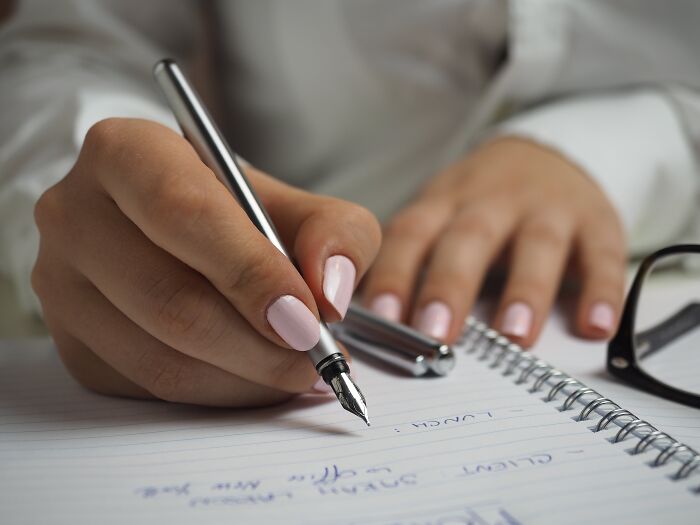 Person writing in notebook with pen, illustrating basic skills challenge.
