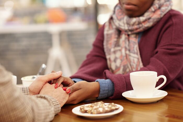 Two people comforting each other over coffee, holding hands.