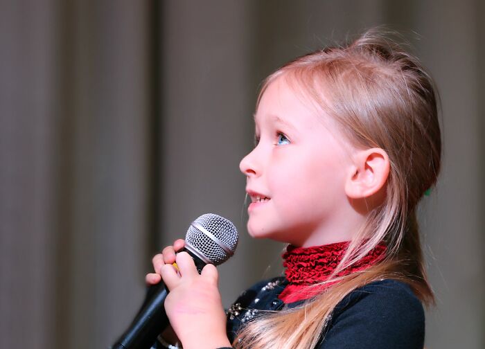 Child holding a microphone, speaking on stage, representing the theme "basic thing you are terrible at."