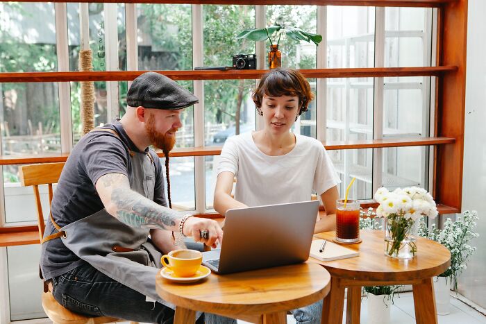 Two people at a café table, one pointing at a laptop, discussing basic skills.