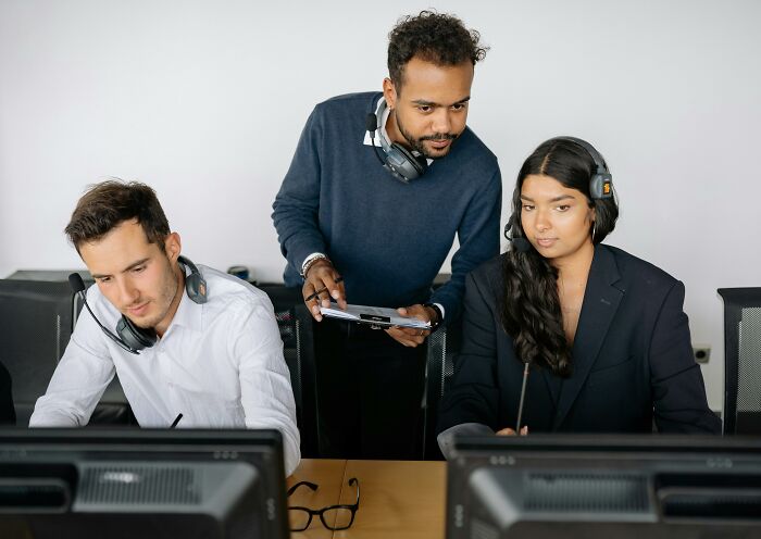 Three people with headsets at computer stations, engaging in teamwork and communication activities.