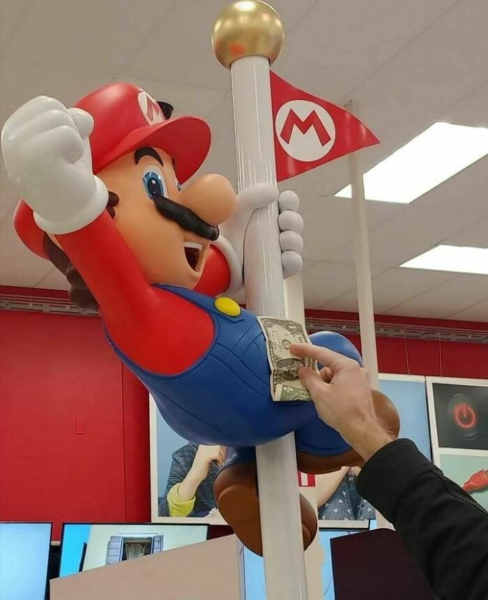 A Mario statue on a pole with a hand holding a dollar, humorously captured.
