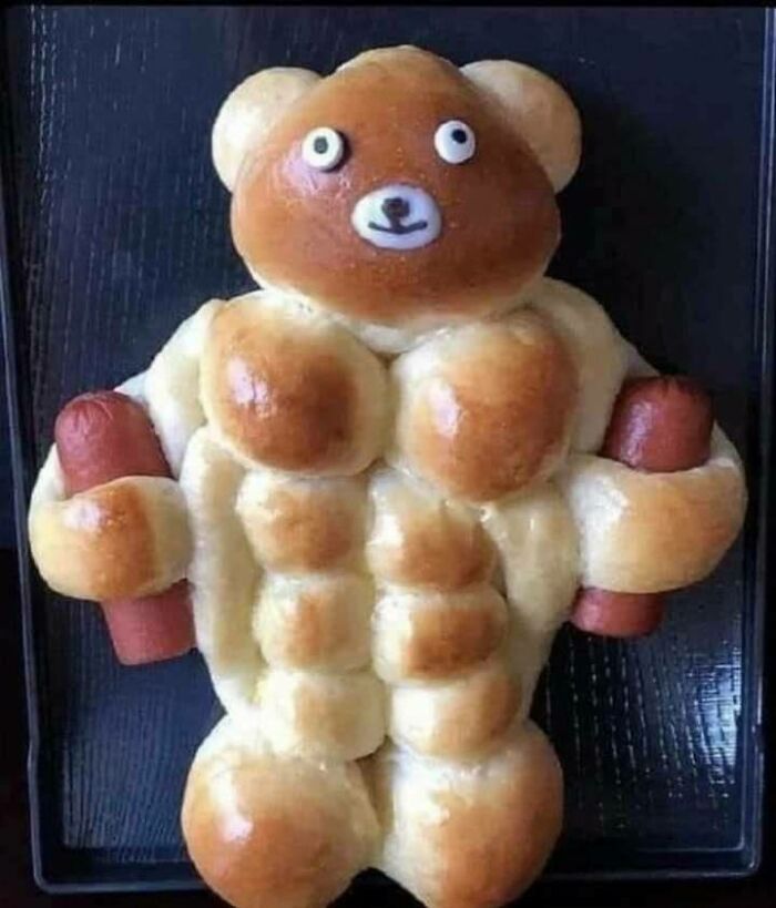 Bread shaped like a muscular teddy bear holding sausages on a tray.