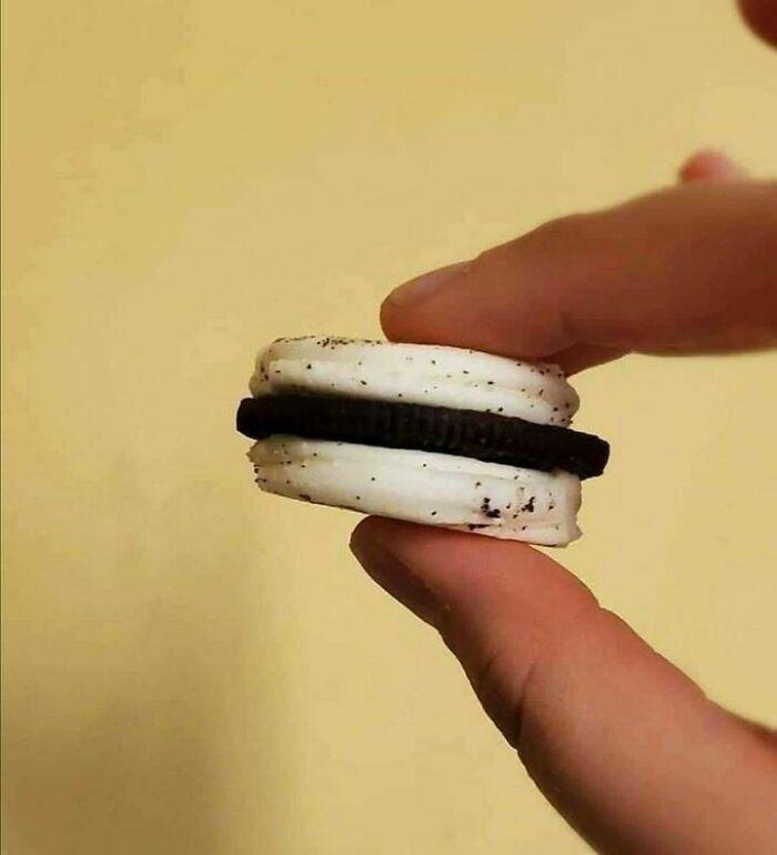 Double-stuffed cookie held between fingers, showcasing a thick layer of creme, creating a hilarious visual.