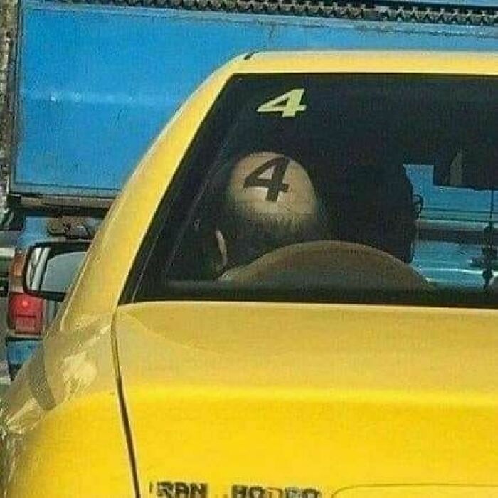 Bald head in car aligns perfectly with number 4 on the window, creating a hilarious image.