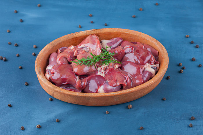 Bowl of raw chicken meal ingredients on a blue background, garnished with fresh herbs.