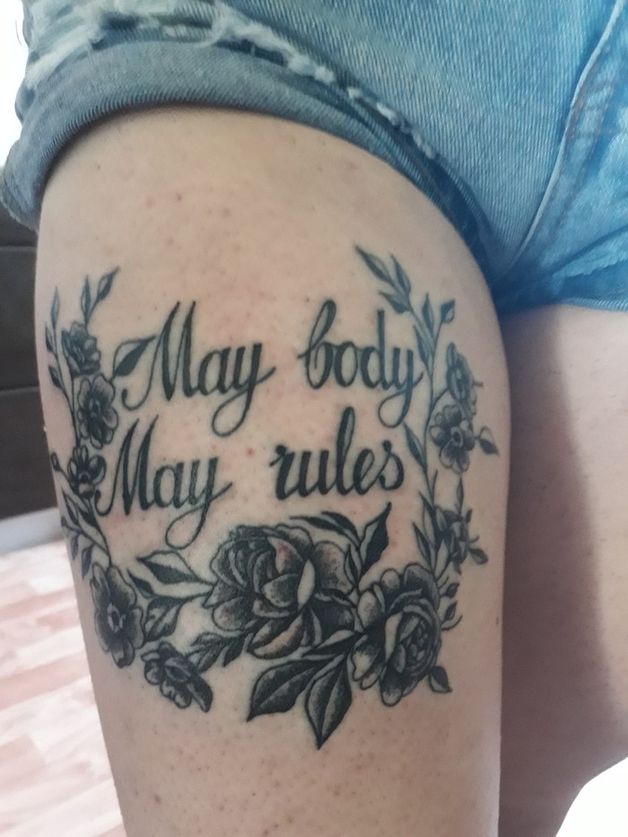 Failed tattoo with misspelled text "May body, May rules" amidst floral design on thigh.