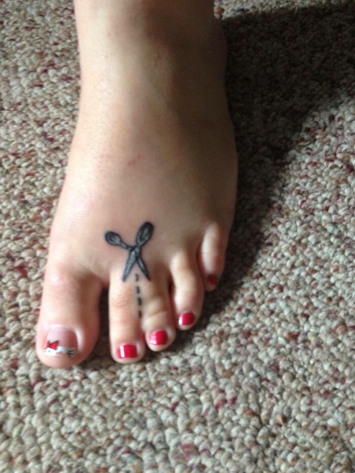 Failed tattoo of scissors and dotted line on a foot with red toenail polish.