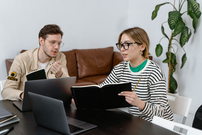 Two people discussing notes at a table with laptops, focusing on a possible affair connected to a lily tattoo. Two people discussing notes at a table with laptops, focusing on a possible affair connected to a lily tattoo.