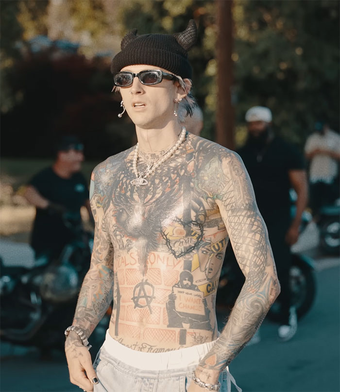 Tattooed Machine Gun Kelly outdoors with sunglasses, wearing a beanie and jewelry, showcasing a bold blackout tattoo. Tattooed Machine Gun Kelly outdoors with sunglasses, wearing a beanie and jewelry, showcasing a bold blackout tattoo.