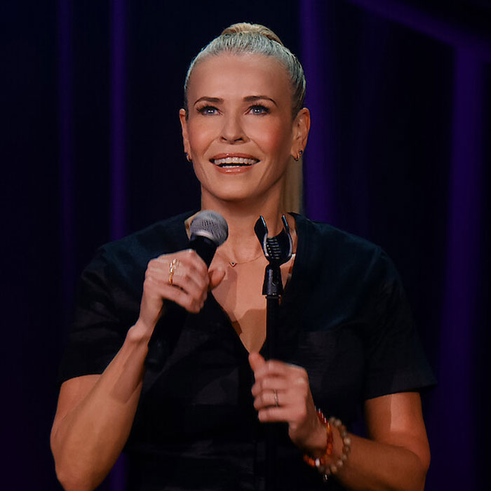 Celebrity smiling while holding a microphone on stage, before cancel culture era.