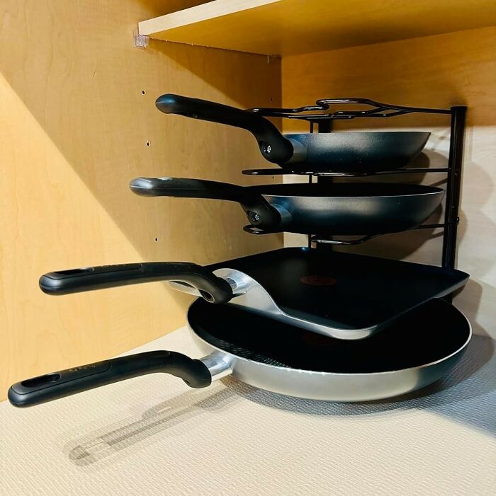 Stacked nonstick frying pans on cabinet rack, kitchen feel like new cookware organization and tidy storage