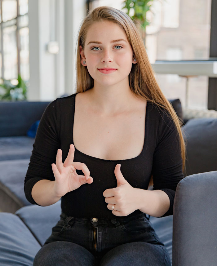Young woman sitting indoors showing fun facts with hand gestures, representing weird and fun facts to know online thread.
