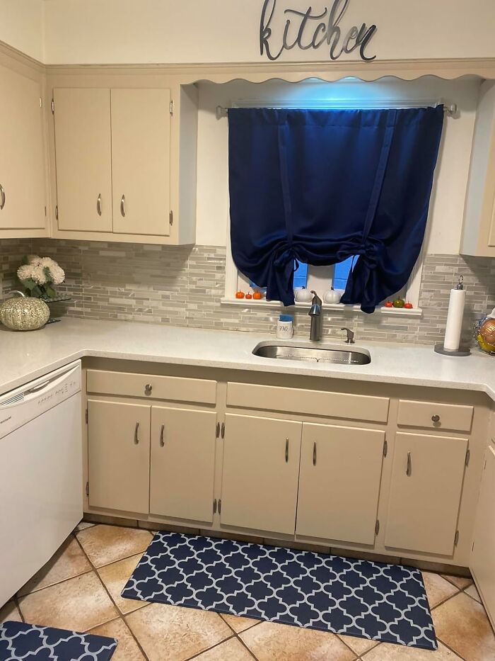 Beige kitchen with navy curtains, quartz countertops, glass tile backsplash and sink, styled to help kitchen feel like new