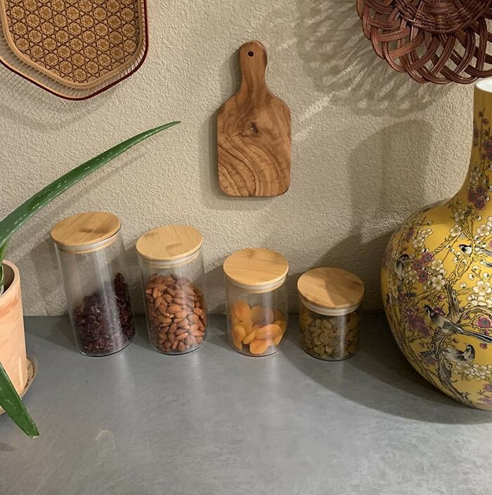 Glass jars of nuts and dried fruit with bamboo lids on countertop, small wood board and yellow vase — kitchen feel like new
