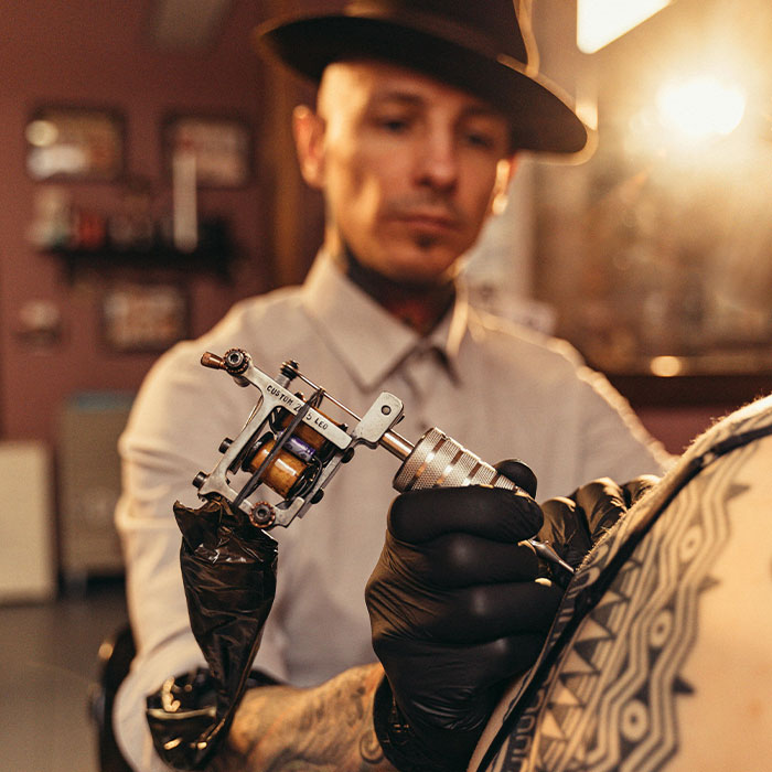 Tattoo artist working on client's arm with ink machine. Tattoo artist working on client's arm with ink machine.