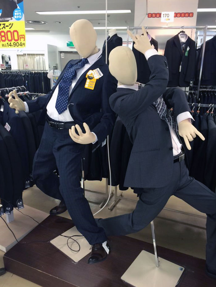Two faceless mannequins in business suits striking dynamic poses in a Japanese clothing store display.