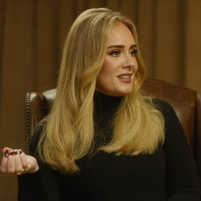 Woman with long blonde hair and black turtleneck discussing famous people accused of plastic surgery in an interview.