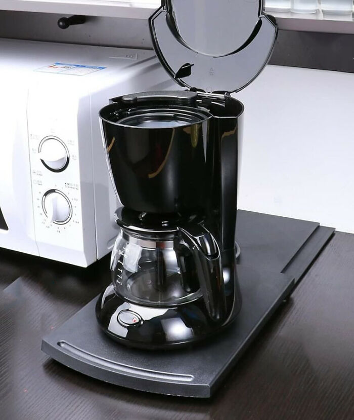 Black drip coffee maker with glass carafe on dark kitchen countertop beside microwave, kitchen feel like new