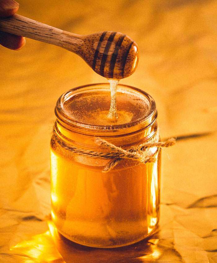 Jar of honey with wooden honey dipper dripping honey, illustrating weird fun facts about honey shared in an online thread.