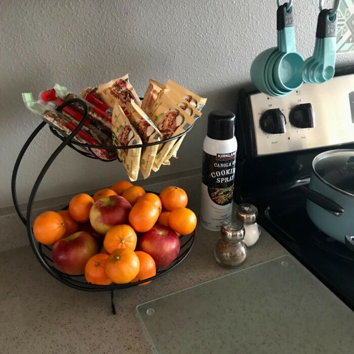 Two-tier fruit stand with apples and tangerines beside stove and measuring cups, kitchen feel like new