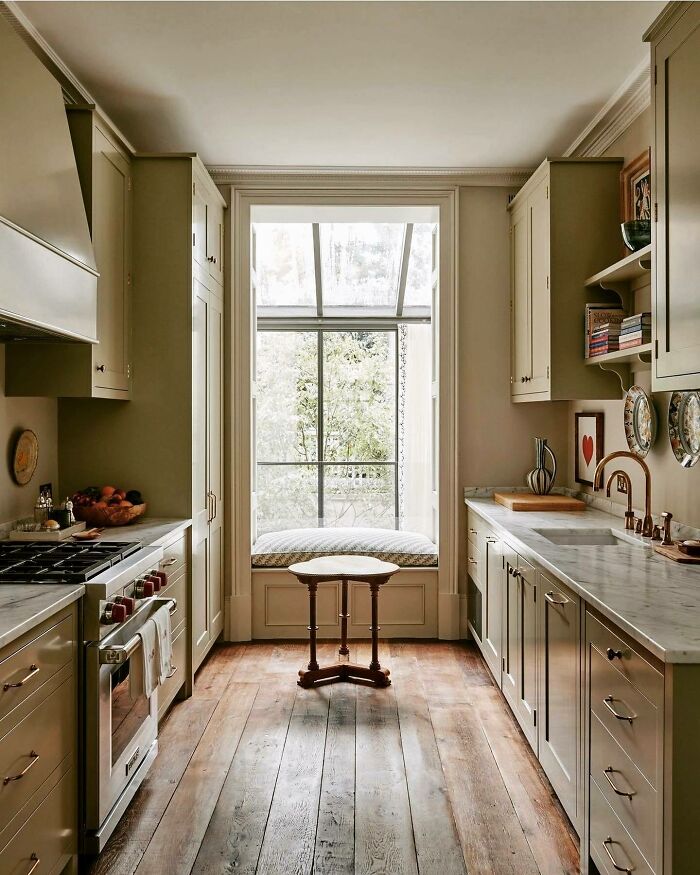 Galley kitchen with neutral cabinets, wooden floors, marble countertops, and a window seat with natural light.