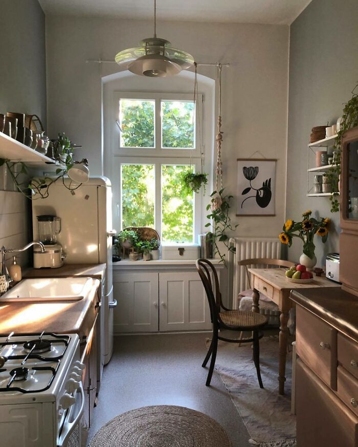 Cozy galley kitchen with wooden countertops, natural light, plants, and vintage furniture in a small space design.