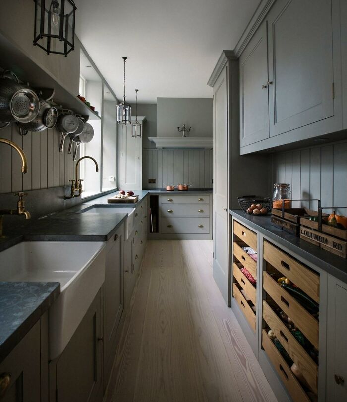 Modern galley kitchen with gray cabinets, wooden storage drawers, and dark countertops in a narrow space design