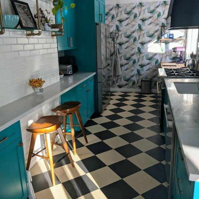 Bright galley kitchen with teal cabinets, black and white checkered floor, and botanical patterned accent wall.