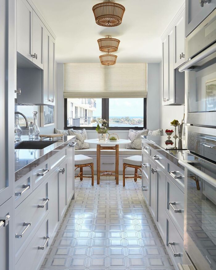 Galley kitchen with white cabinets, black countertops, wicker lighting, and a cozy dining nook with a city view.