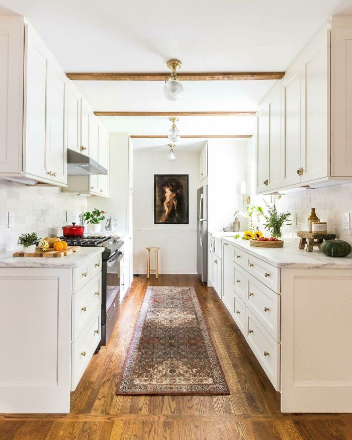 Bright galley kitchen with white cabinets, marble countertops, wood floors, and decorative rug showcasing small space design ideas.