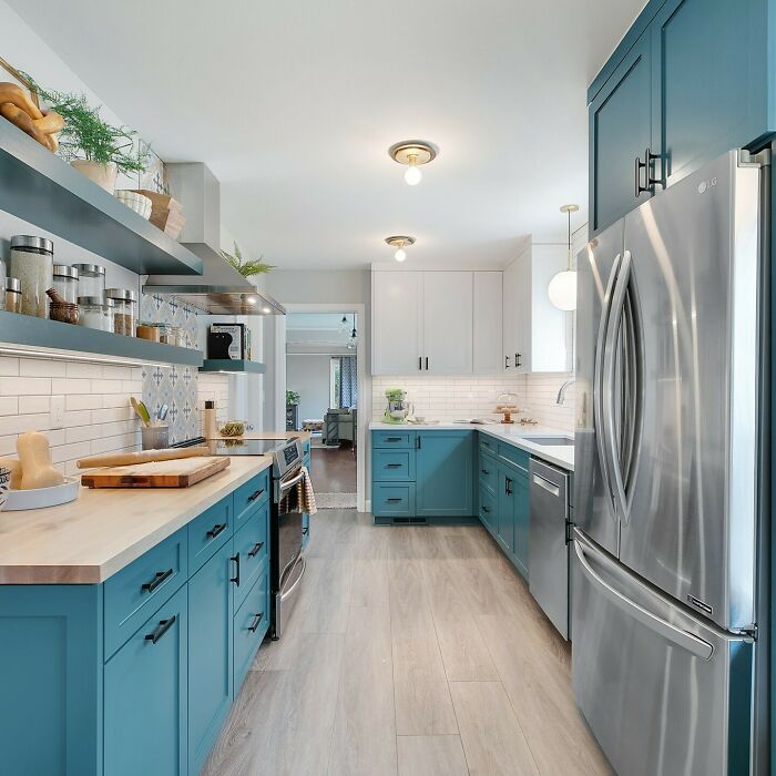 Modern galley kitchen with blue cabinets, stainless steel appliances, and open shelving in a small space design.