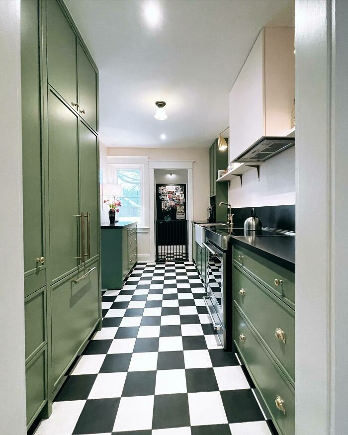 Galley kitchen with green cabinets, black countertops, and checkered black and white floor in a small space design.