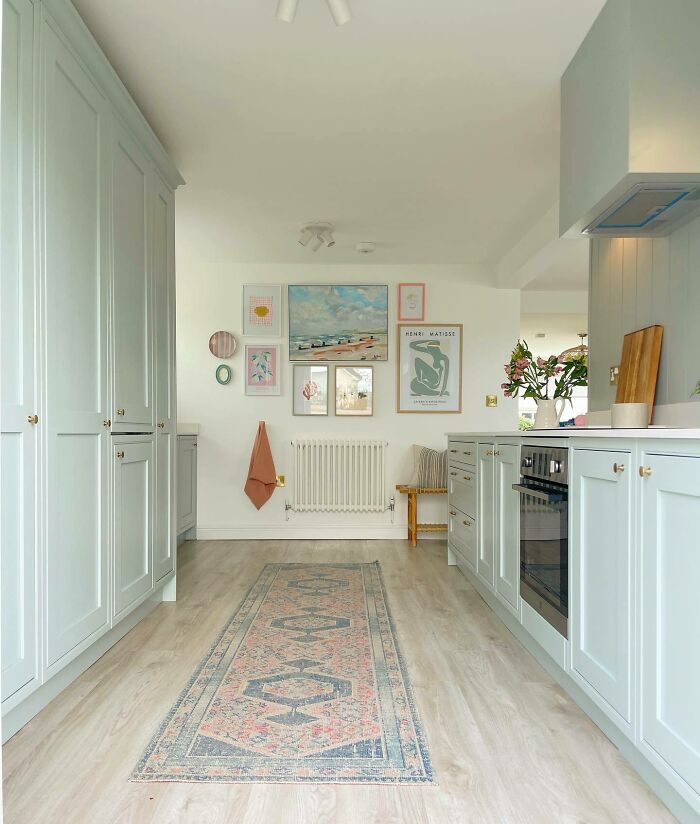 Bright galley kitchen with light blue cabinetry, wall art, and a patterned runner showcasing galley kitchen ideas in small spaces.