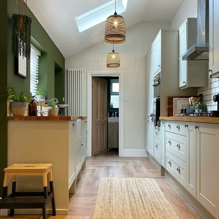 Galley kitchen with white cabinets, wooden countertops, green accent wall, pendant lights, and natural light from skylight.