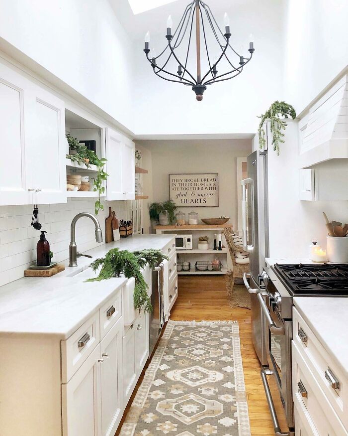 Bright and cozy galley kitchen with white cabinets, marble countertops, stainless steel appliances, and decorative greenery accents.