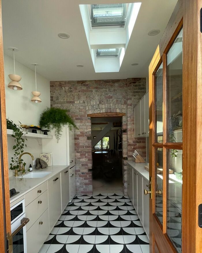 Bright galley kitchen with skylights, patterned tile floor, white cabinetry, and exposed brick wall in small space design.