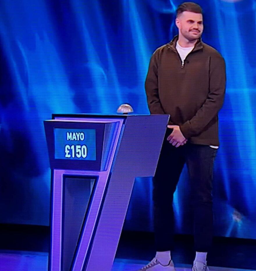 Man stands by podium on quiz show with amusingly unfortunate name displayed, earning £150.