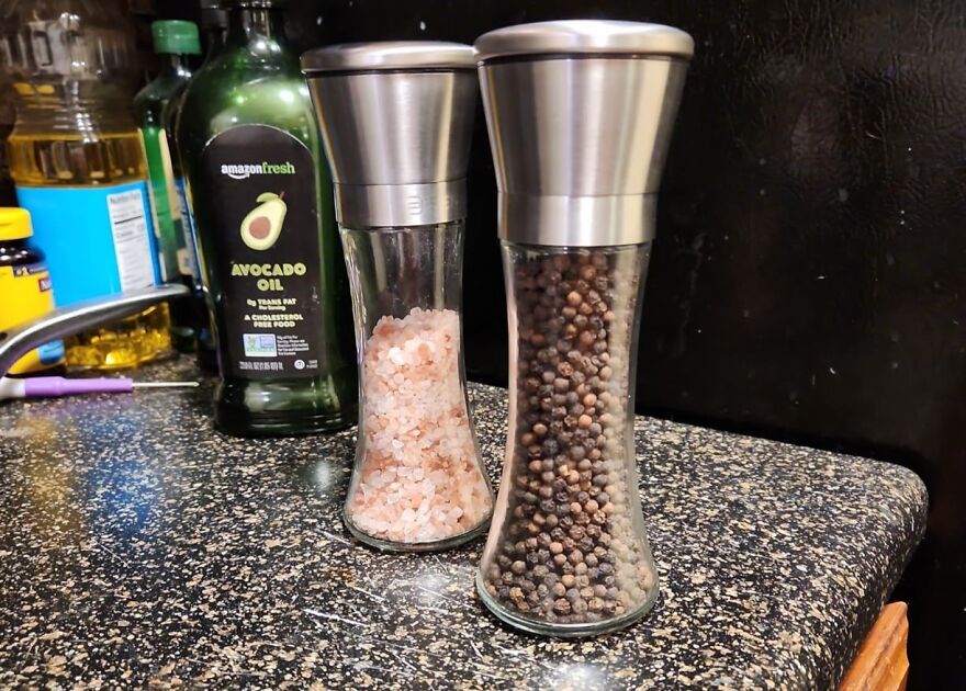 Two glass salt and pepper grinders on speckled countertop with oil bottle behind, kitchen feel like new
